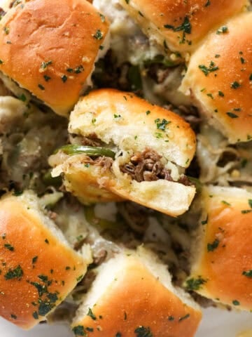 Overhead close up view of philly cheesesteak sliders with one slider turned on its side.