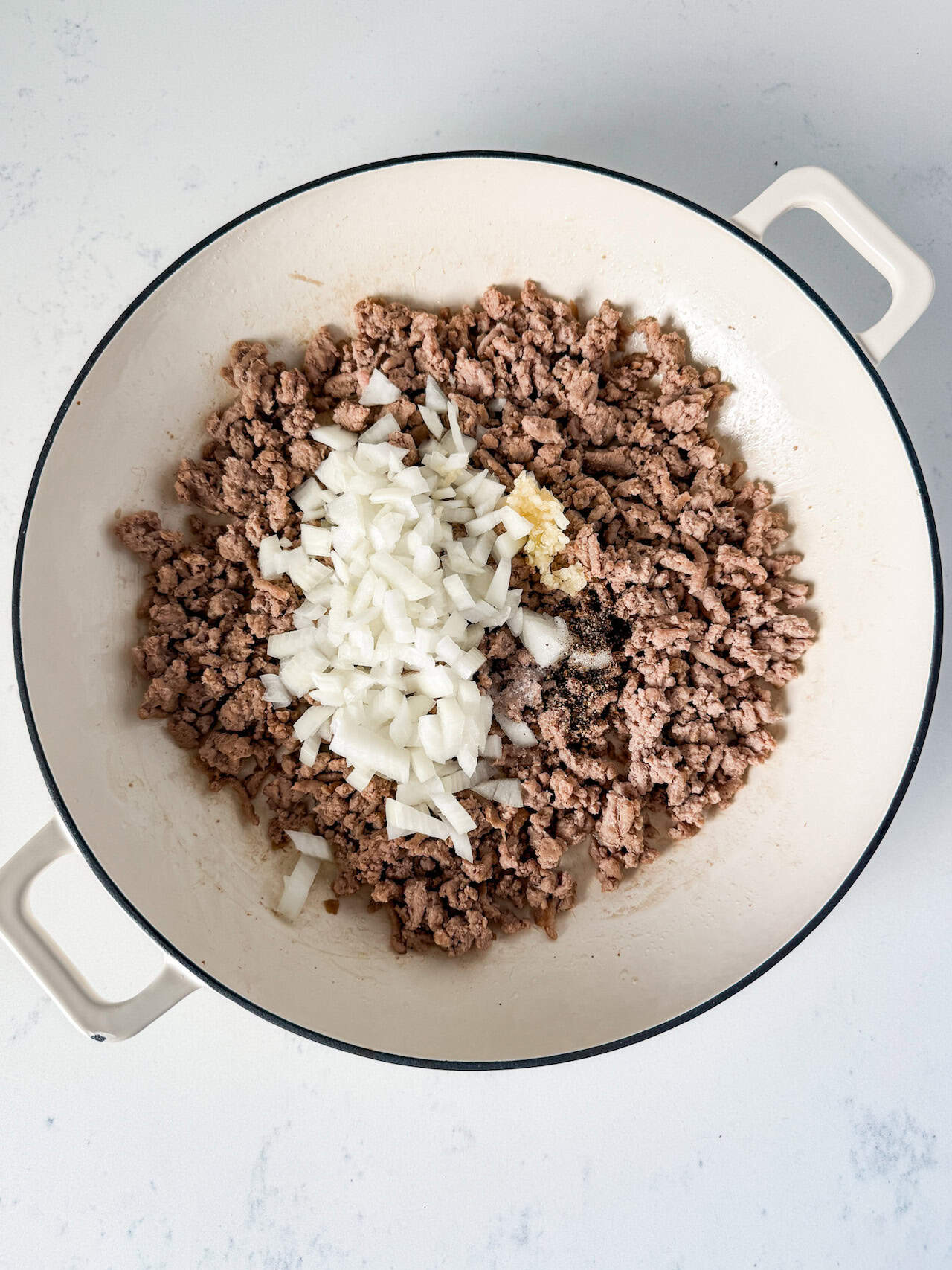 Onion and minced garlic being added to the skillet.