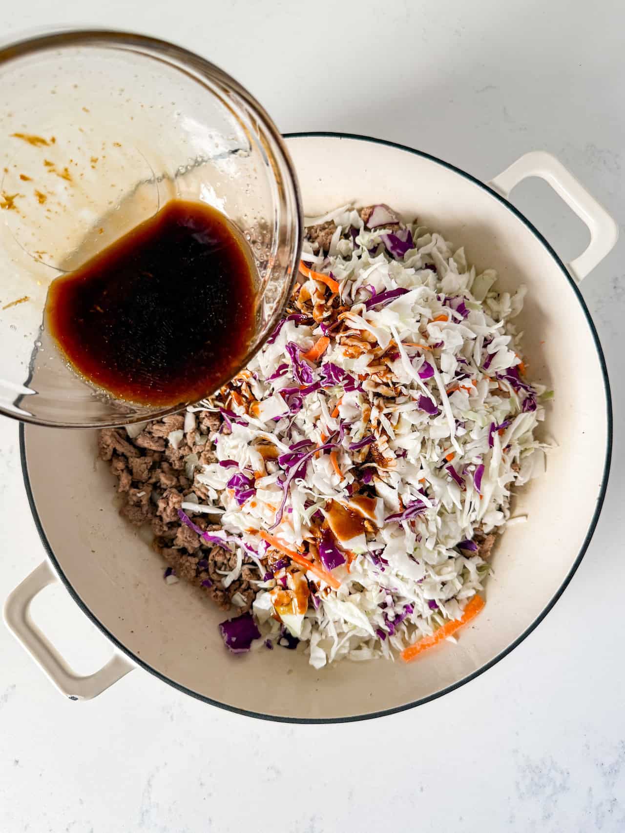 Coleslaw and stir-fry sauce being added to the skillet.