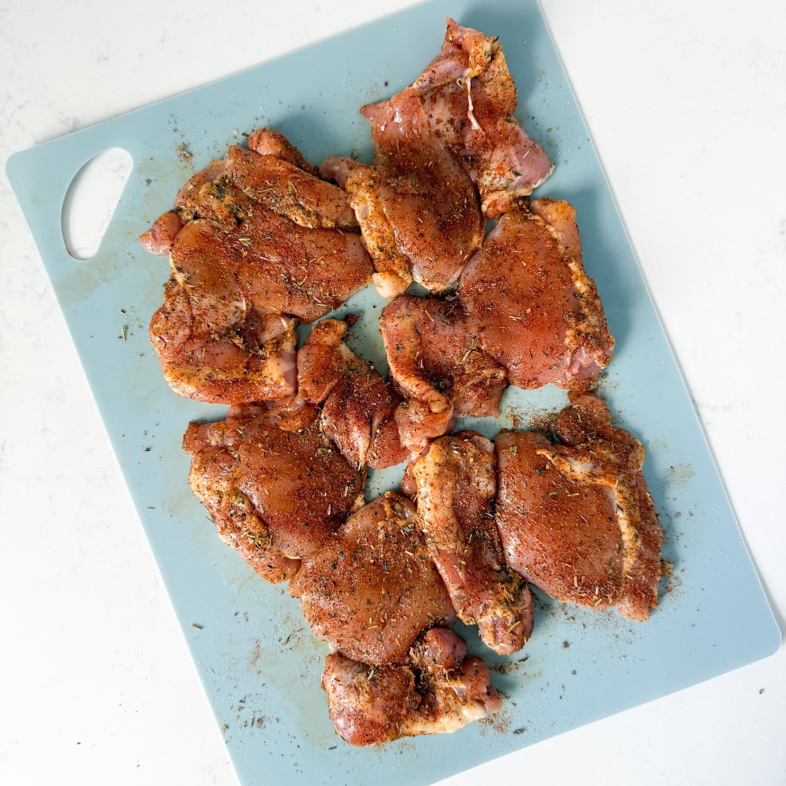 Seasoned boneless skinless chicken thighs on a cutting board.