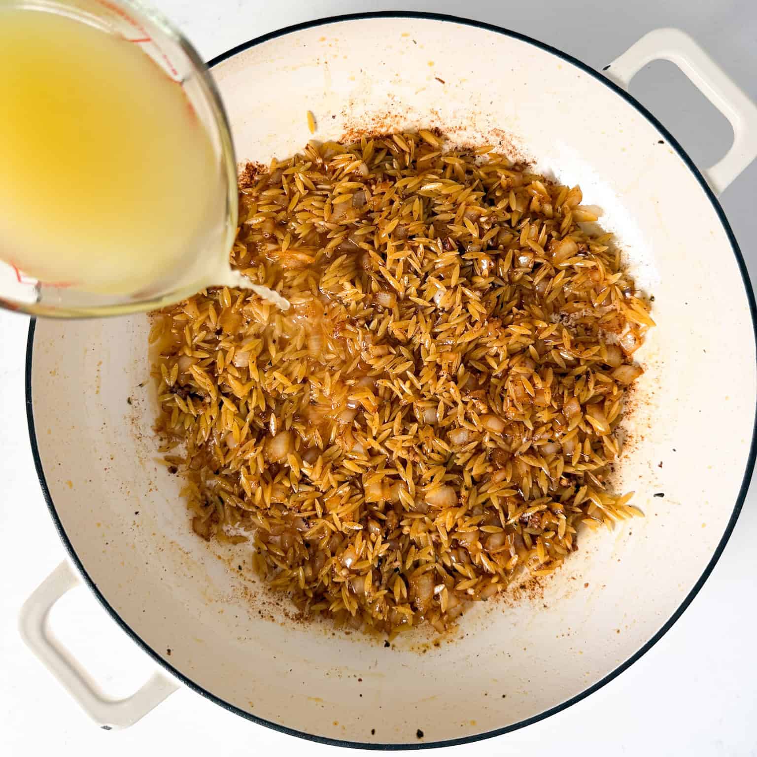 Sauteed onions, garlic, orzo, and chicken broth added to skillet.