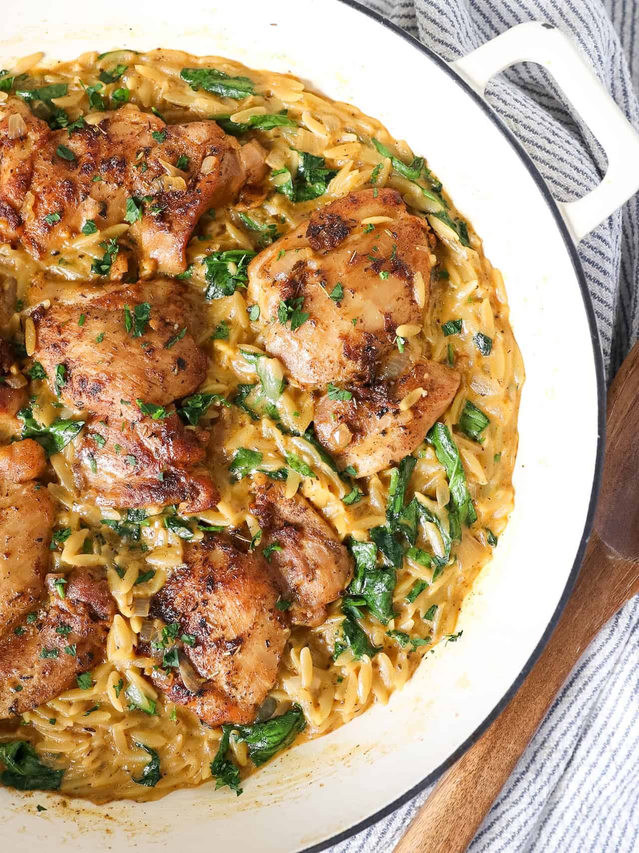 Overhead view of creamy chicken and orzo pasta in a white cast iron skillet.