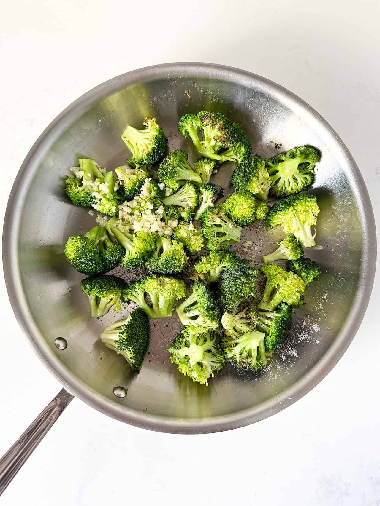 Garlic, salt, and black pepper added to broccoli in a skillet.