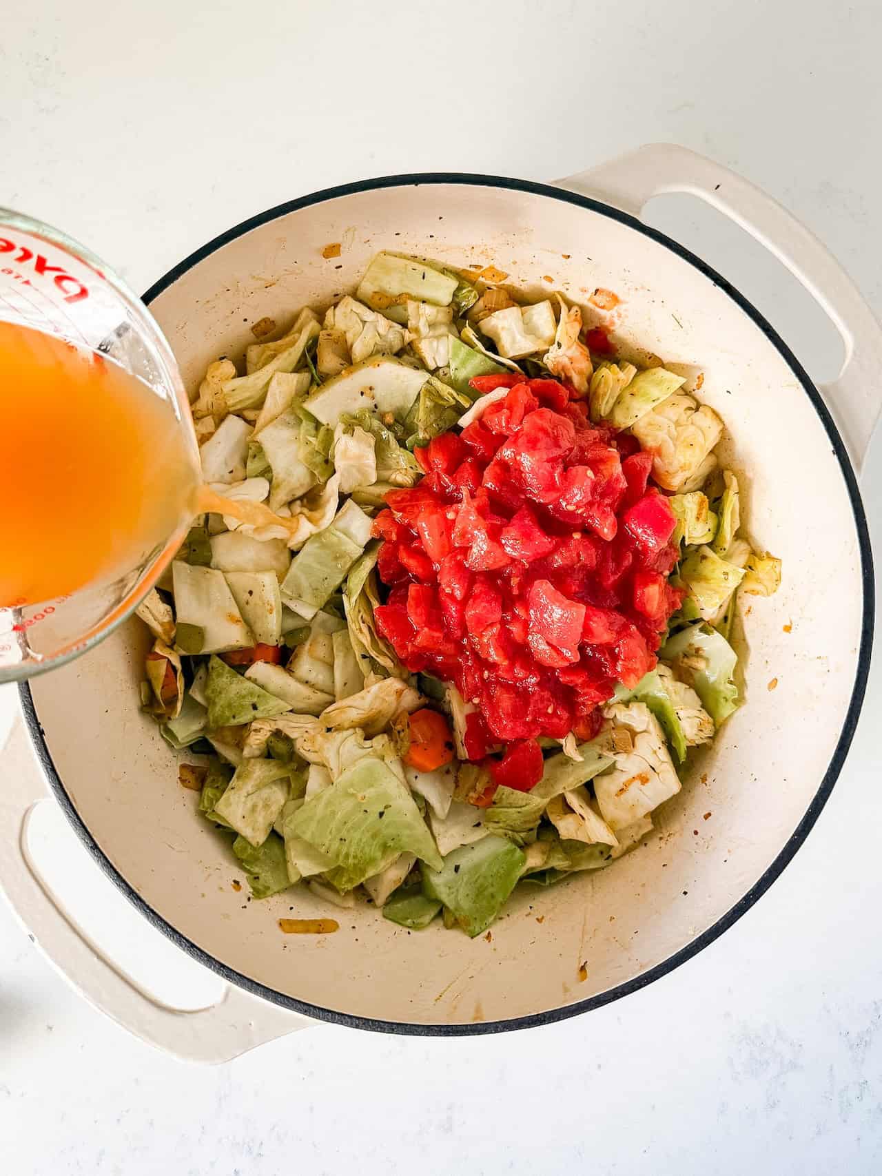 Diced tomatoes and vegetable broth being added to the pot.