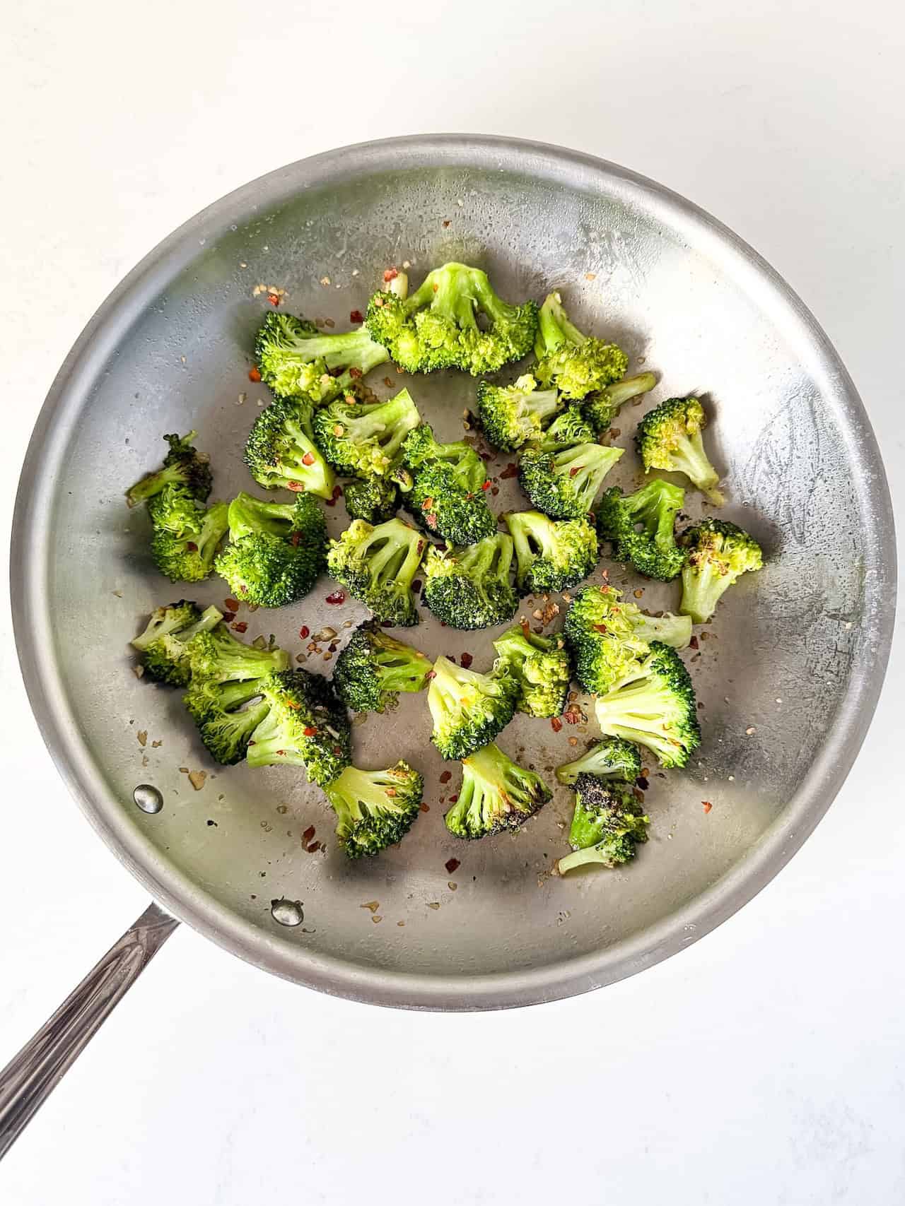 Sautéed broccoli in a skillet with crushed red pepper on top.