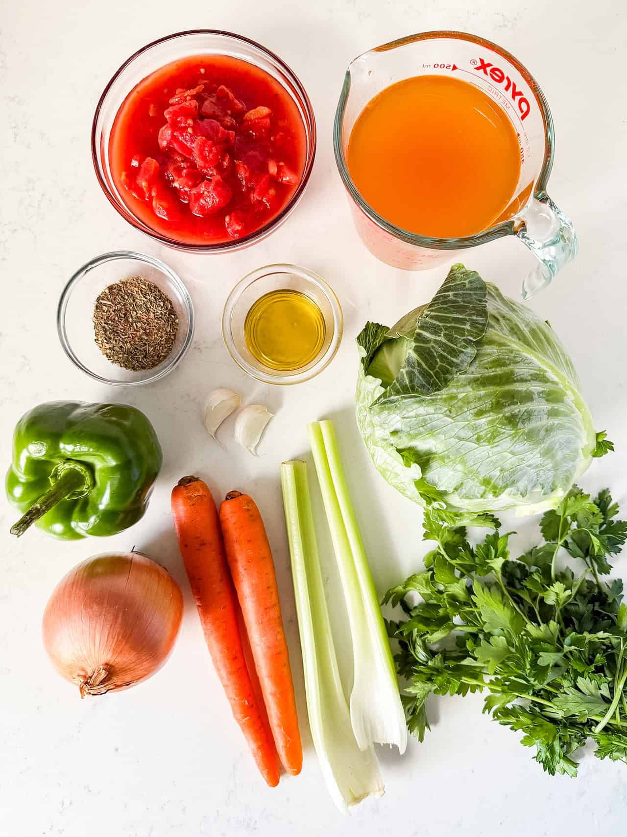 Overhead view of the ingredients for cabbage soup on a white countertop.