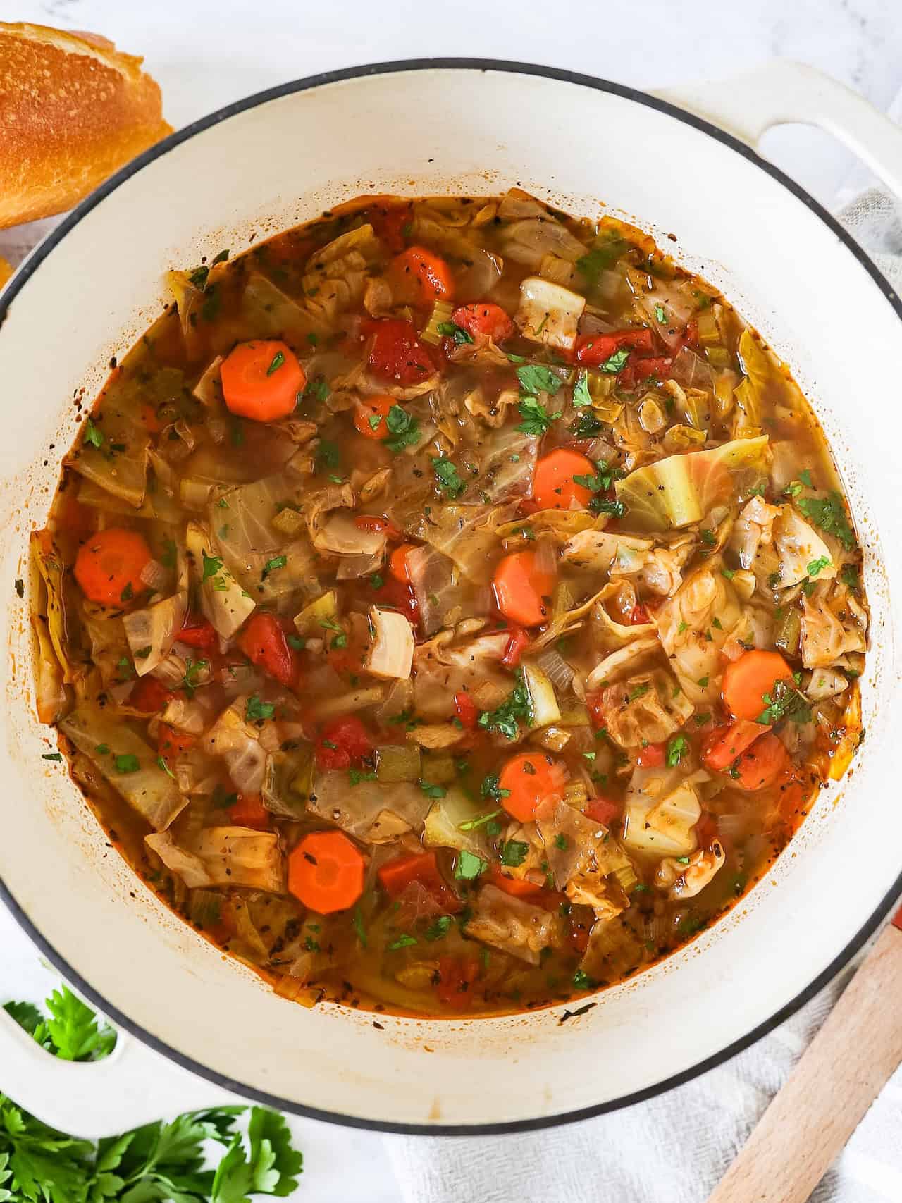 Overhead view of cabbage soup in a dutch oven pot with parsley and bread on the side.