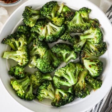 Overhead view of sautéed broccoli in a white serving dish with a napkin on the side.