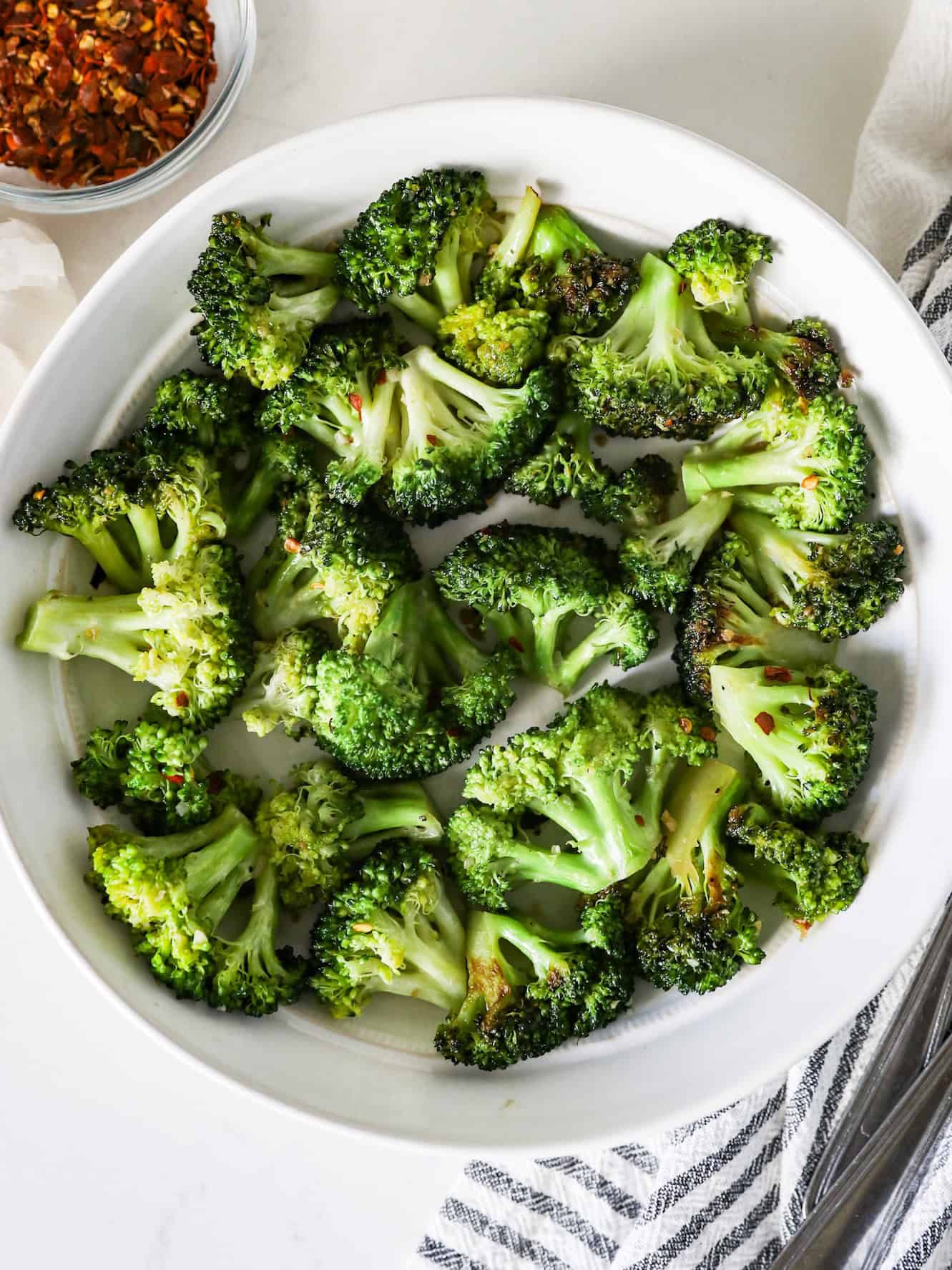 Overhead view of sautéed broccoli in a white serving dish with a napkin on the side.