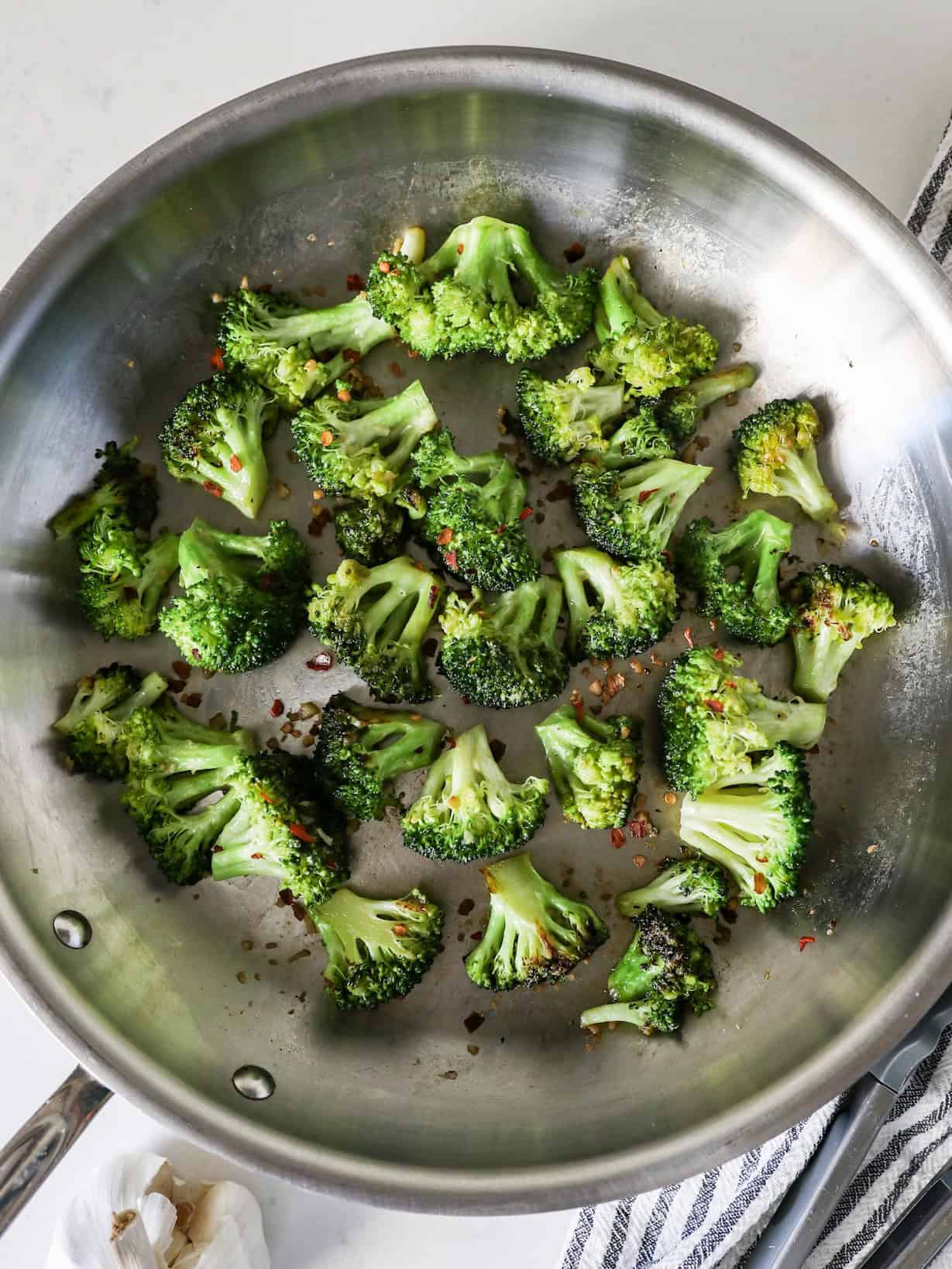 Overhead view of sautéed broccoli in a skillet with crushed red pepper on top.