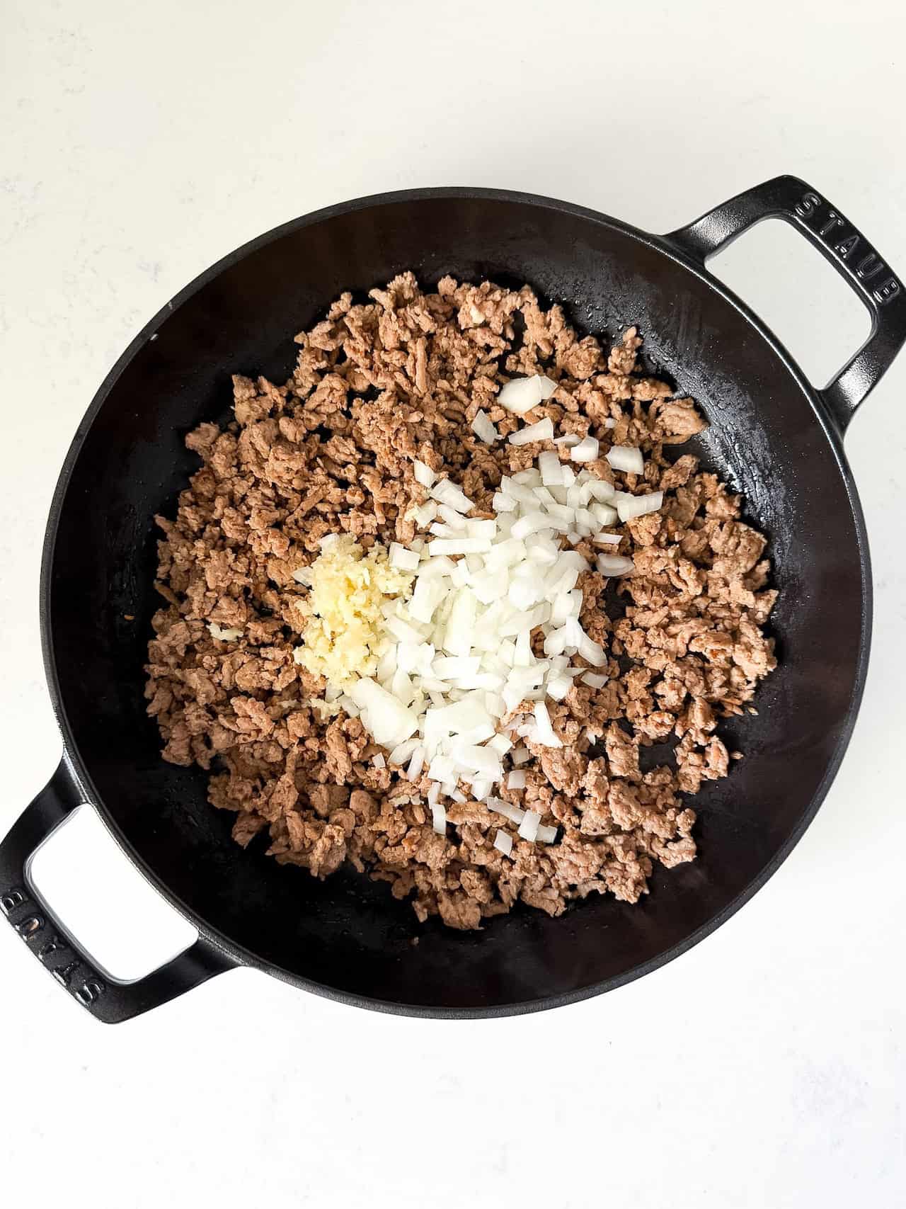 Cooked Italian sausage in a skillet with diced onion and garlic added.
