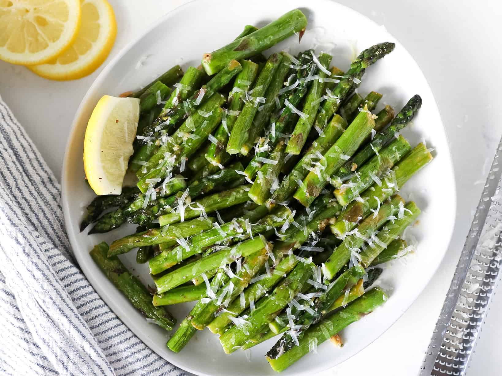 Overhead view of sautéed asparagus in a white serving dish with grated parmesan on top.