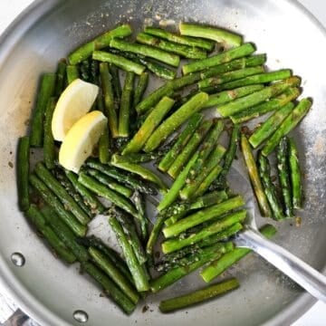 Overhead view of sautéed asparagus in a stainless steel skillet.