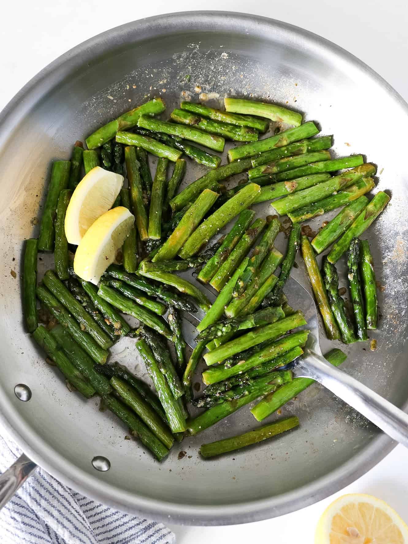 Overhead view of sautéed asparagus in a stainless steel skillet.