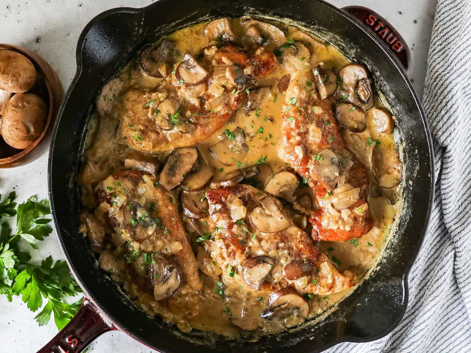 Overhead view of creamy mushroom chicken in a cast iron skillet with a napkin on the side.