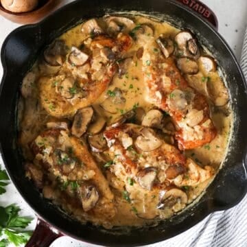 Overhead view of creamy mushroom chicken in a cast iron skillet with a napkin on the side.
