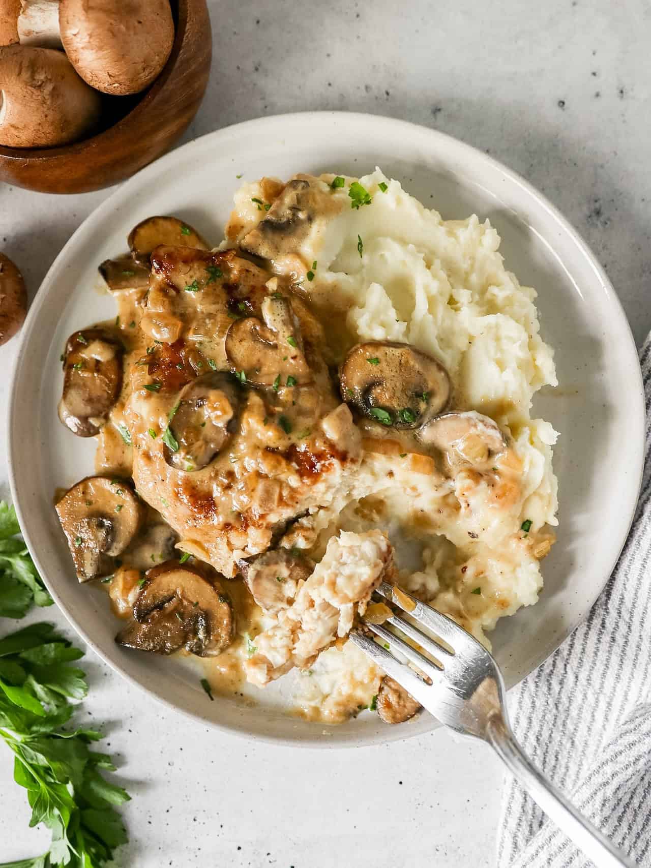 Overhead view of a serving of creamy mushroom chicken on a plate with mashed potatoes and a piece of chicken on a fork.