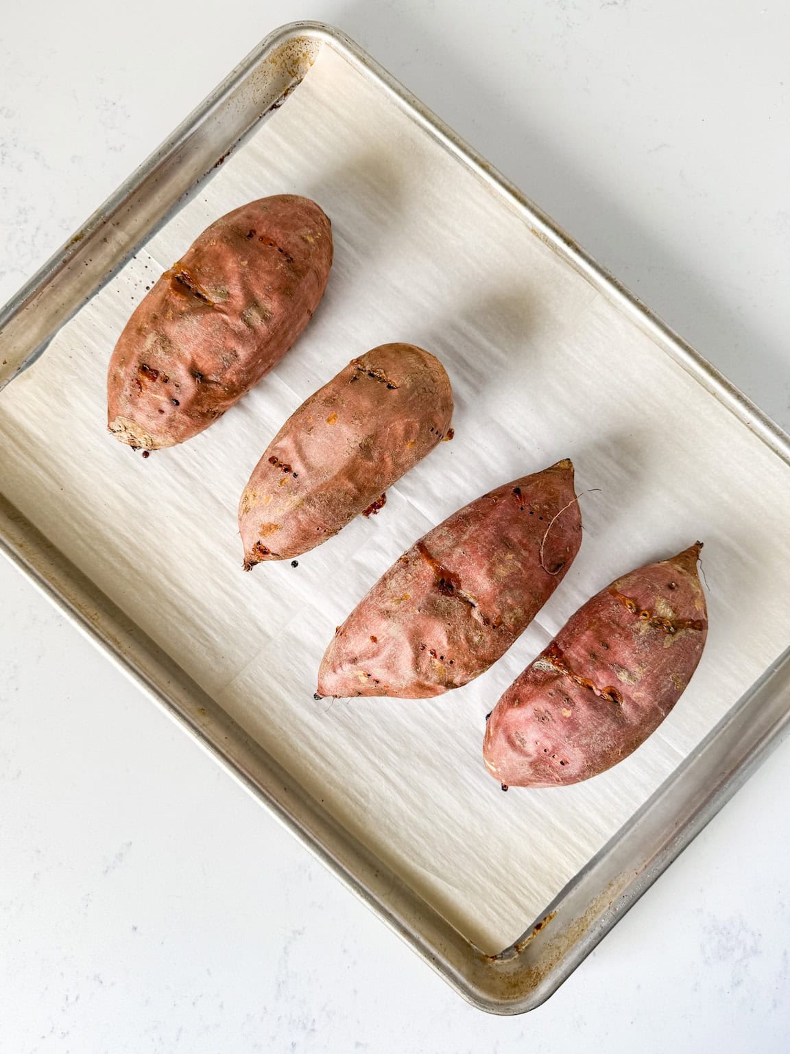 Baked sweet potatoes on a parchment lined baking sheet.