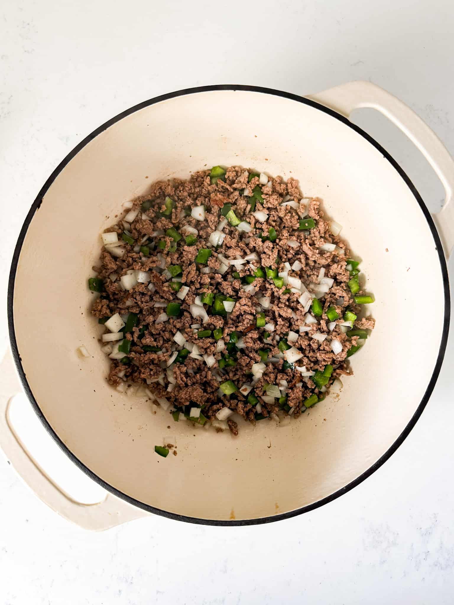 Browned ground beef with onions and bell peppers in a pot.