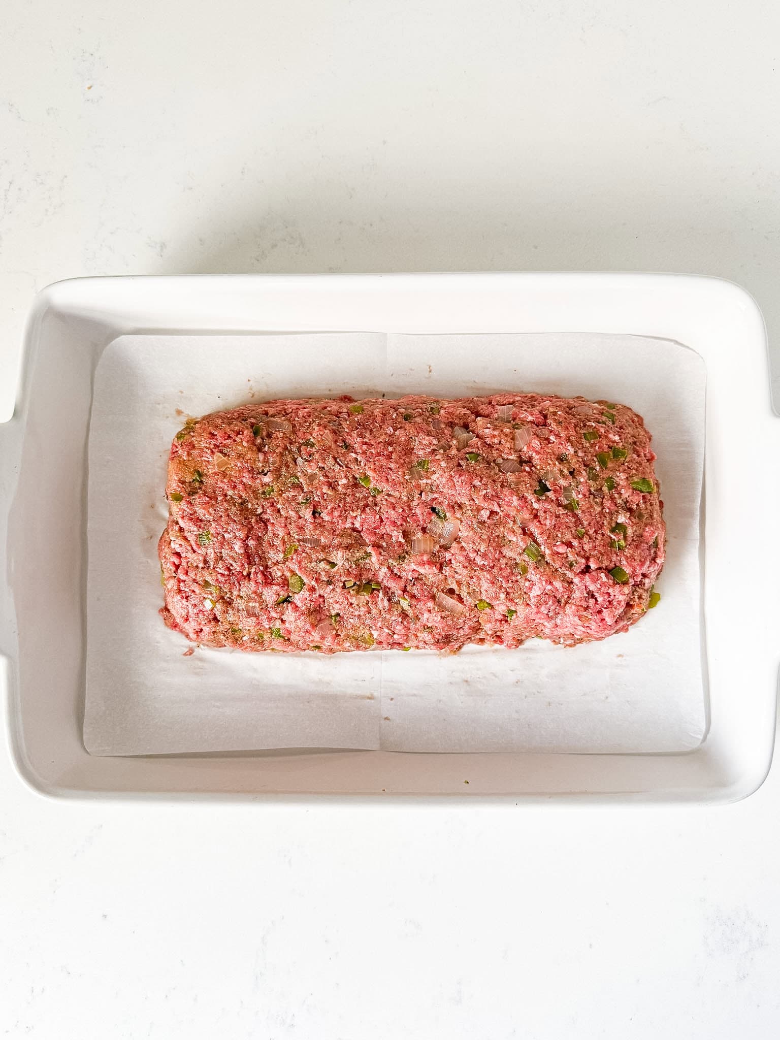 Meatloaf shaped into a loaf and placed in a white baking dish.