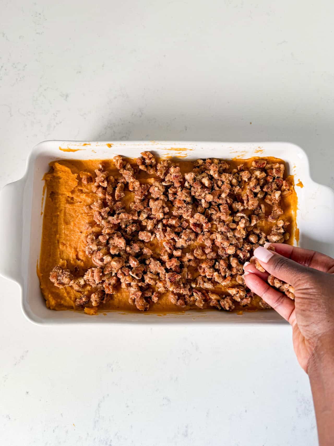 Pecans being added on top of sweet potato casserole.