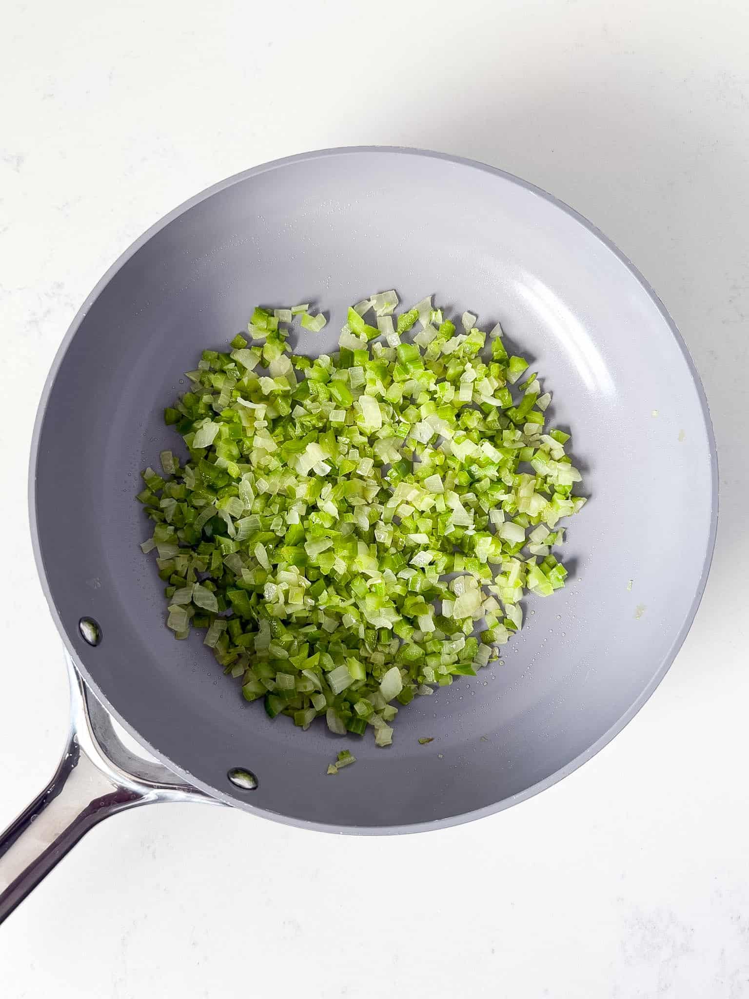 Sautéed onions, celery, and bell pepper in a skillet.