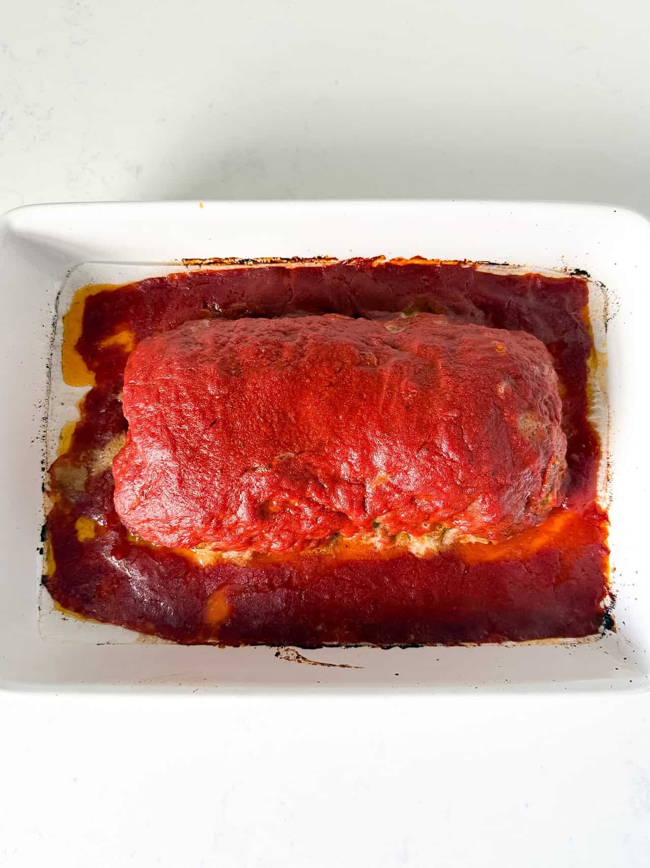 Cooked oven baked meatloaf in a white baking dish.