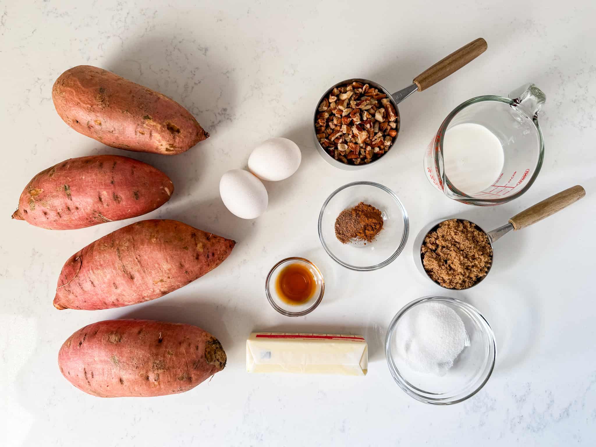 Overhead view of ingredients for sweet potato casserole on a white countertop.