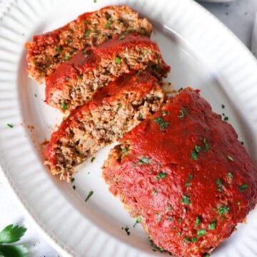 Overhead view of homemade meatloaf on a white plater, sliced into slices.