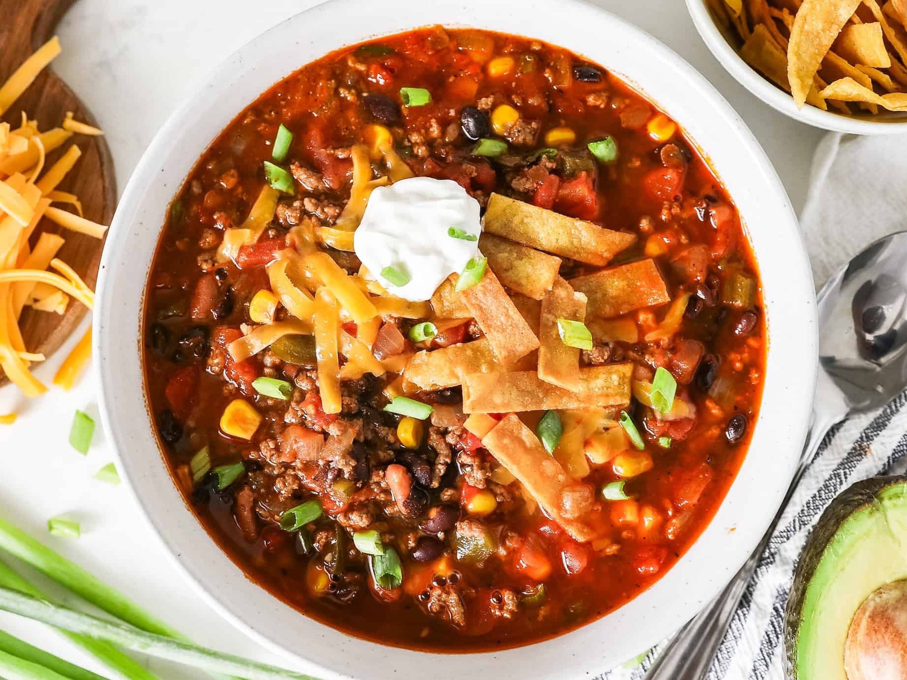 Overhead view of taco soup in a bowl with green onions, a napkin, and a spoon on the side.