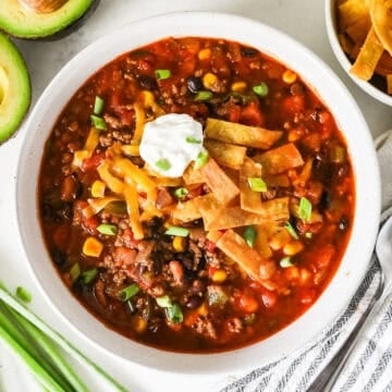 Overhead view of taco soup in a bowl with green onions, a napkin, and a spoon on the side.