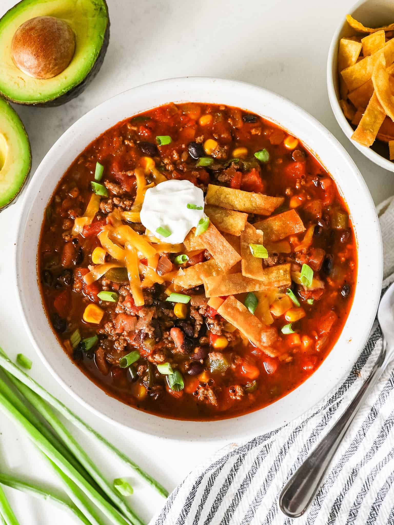 Overhead view of taco soup in a bowl with green onions, a napkin, and a spoon on the side.