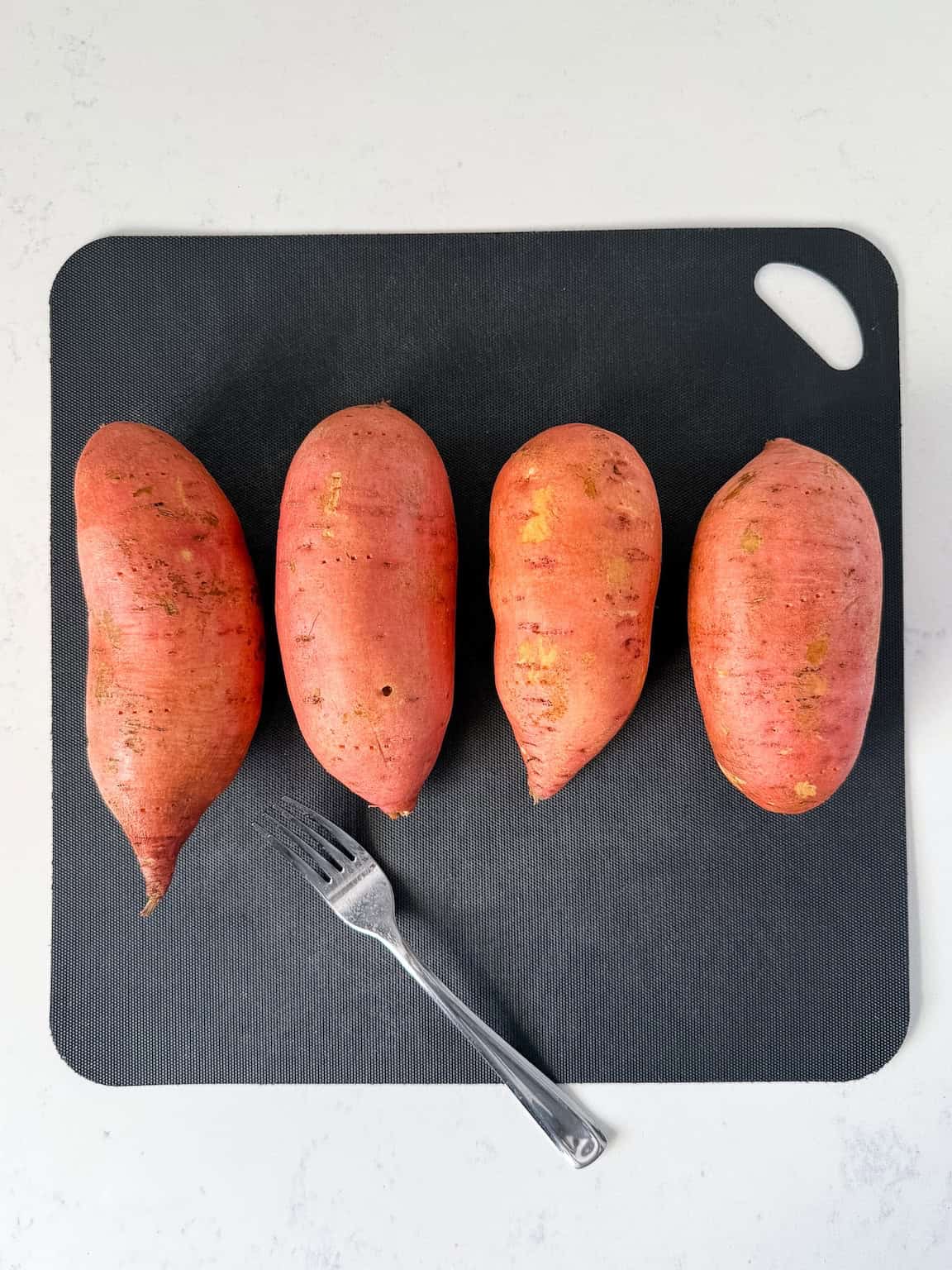 Washed and pricked sweet potatoes on a cutting board