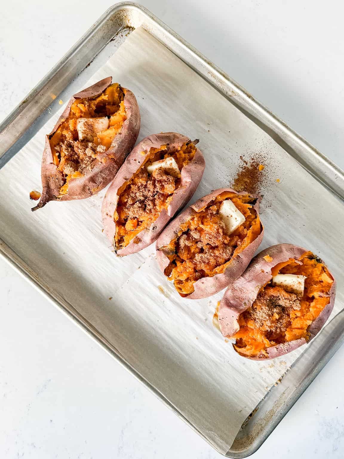 Baked sweet potatoes cut open with butter and brown sugar added in the center.