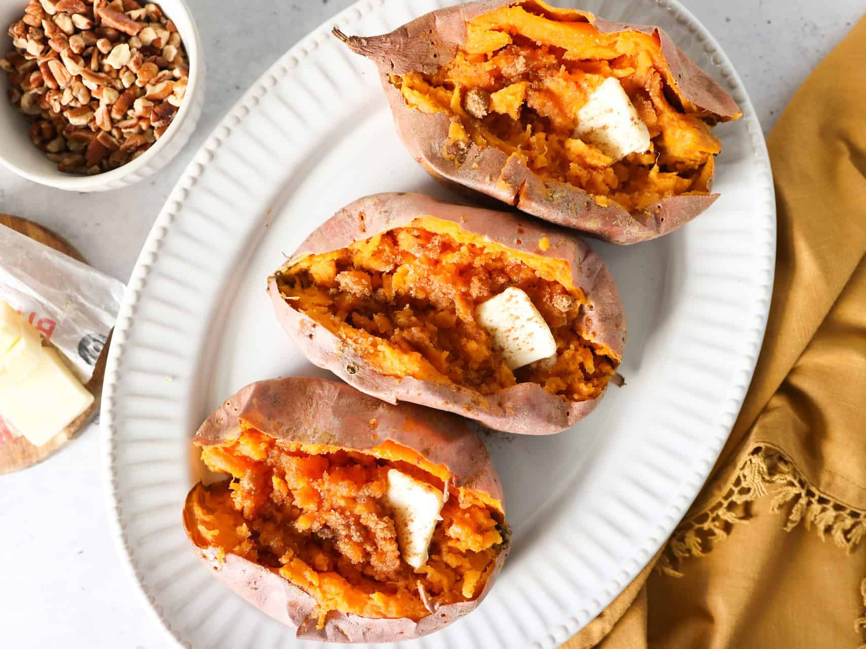 Overhead view of baked sweet potatoes on a white platter with a napkin on the side.