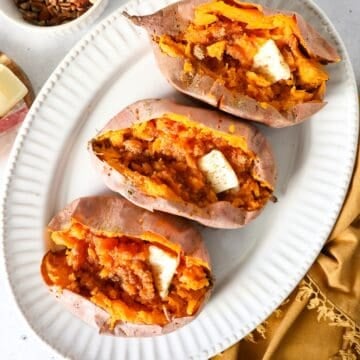 Overhead view of baked sweet potatoes on a white platter with a napkin on the side.